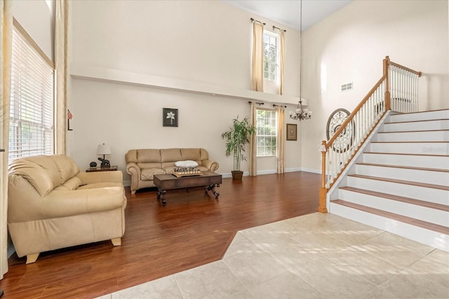 living area with a notable chandelier, a high ceiling, wood finished floors, visible vents, and stairs