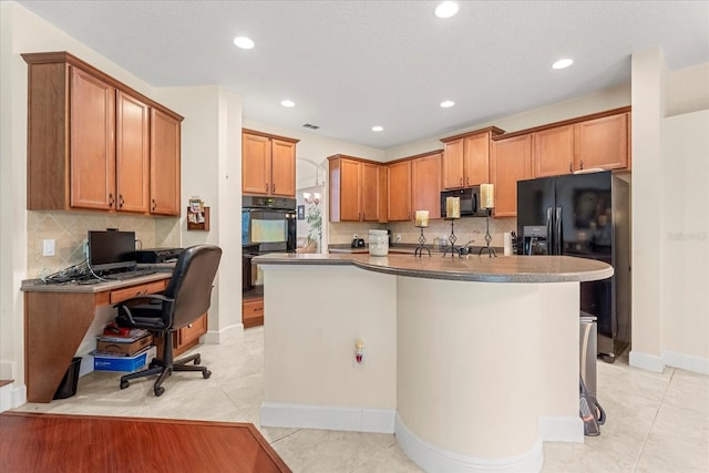 kitchen with dark countertops, brown cabinetry, light tile patterned flooring, an island with sink, and black appliances