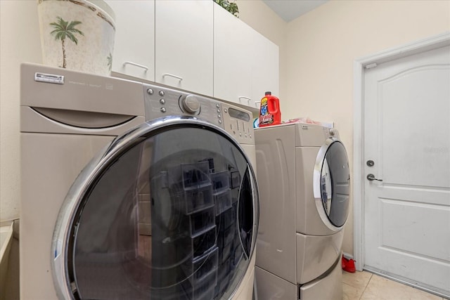 clothes washing area featuring cabinet space, light tile patterned floors, and washer and dryer