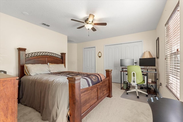 bedroom with visible vents, light colored carpet, ceiling fan, a textured ceiling, and multiple closets