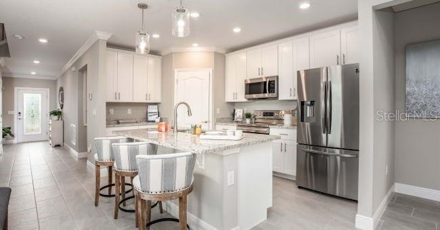 kitchen with stainless steel appliances, ornamental molding, white cabinets, an island with sink, and a kitchen bar