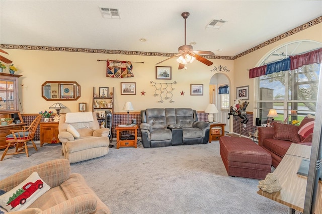 carpeted living room featuring a ceiling fan, arched walkways, and visible vents