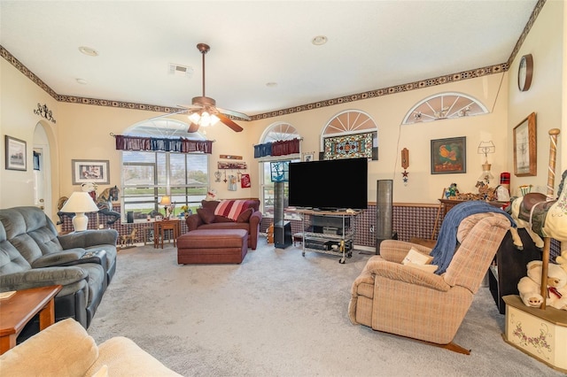 carpeted living room with a ceiling fan, arched walkways, and visible vents