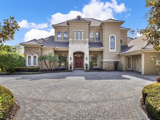 mediterranean / spanish-style house featuring decorative driveway, stone siding, a tiled roof, and stucco siding