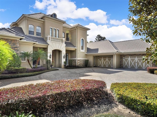 mediterranean / spanish house featuring a balcony, a garage, a tile roof, decorative driveway, and stucco siding