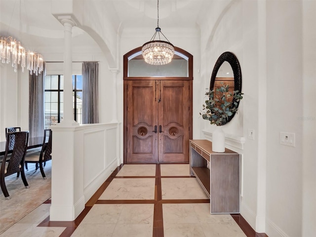 entryway featuring marble finish floor, crown molding, a notable chandelier, a decorative wall, and baseboards