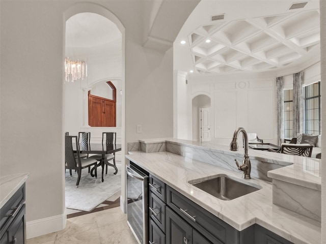 kitchen featuring light stone counters, visible vents, a sink, beverage cooler, and coffered ceiling