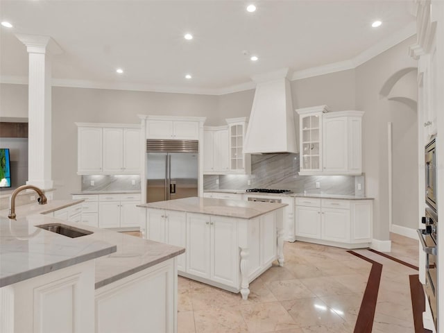 kitchen with a large island, custom exhaust hood, ornamental molding, a sink, and built in appliances