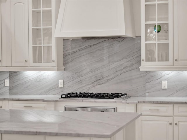 kitchen with glass insert cabinets, gas cooktop, white cabinets, and custom exhaust hood