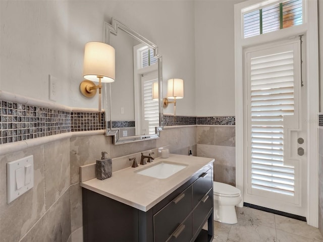 half bathroom with toilet, marble finish floor, tile walls, and vanity