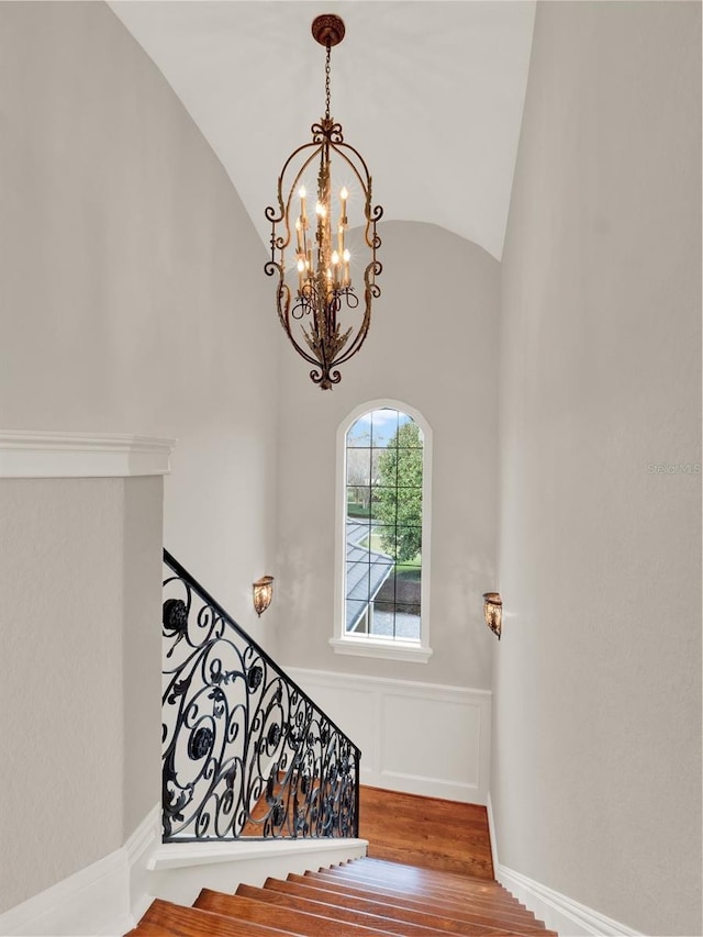 staircase featuring lofted ceiling, a decorative wall, wood finished floors, baseboards, and wainscoting