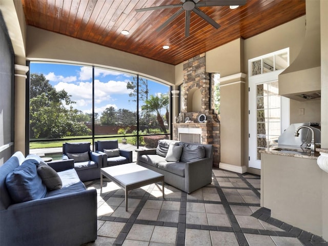 sunroom featuring an outdoor stone fireplace, wooden ceiling, a sink, and a ceiling fan