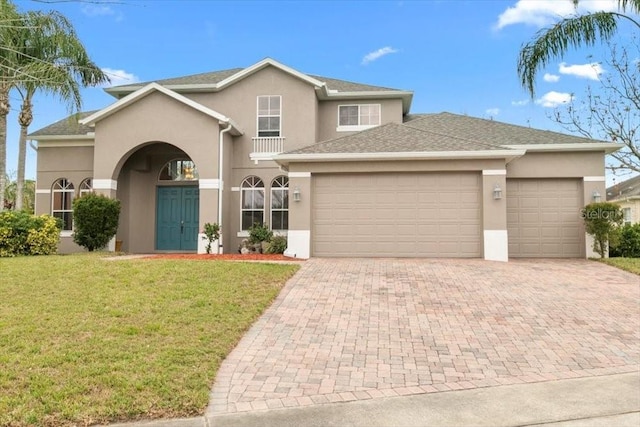 view of front facade with a garage, decorative driveway, a front lawn, and stucco siding