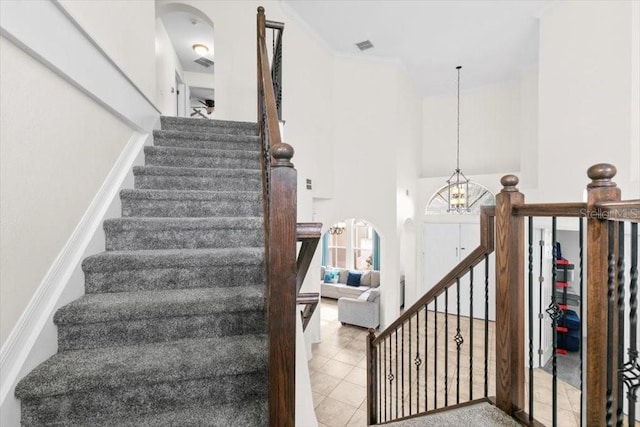 stairs featuring crown molding, a high ceiling, an inviting chandelier, and tile patterned floors