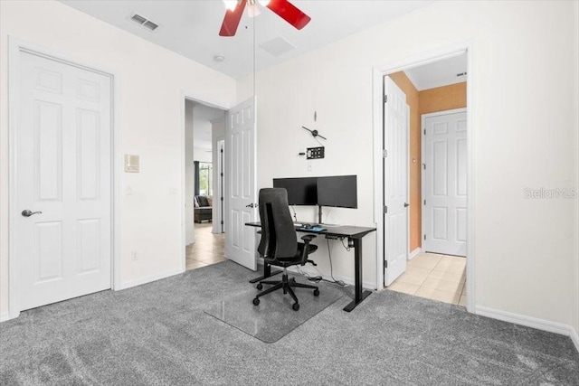 carpeted office space with ceiling fan, visible vents, baseboards, and tile patterned floors