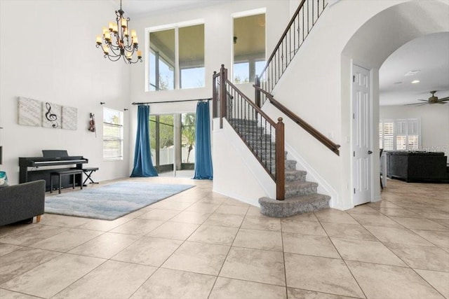 tiled foyer entrance with stairs, ceiling fan with notable chandelier, arched walkways, and a towering ceiling