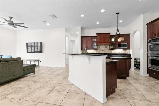 kitchen with an island with sink, dark countertops, open floor plan, stainless steel appliances, and backsplash