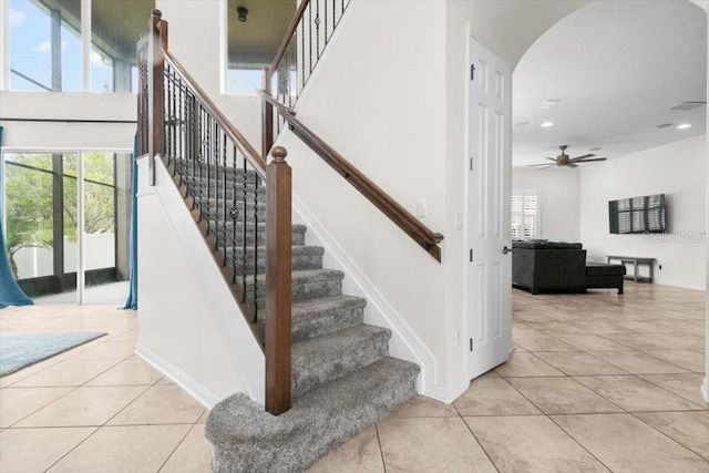 stairs with arched walkways, a towering ceiling, baseboards, and tile patterned floors