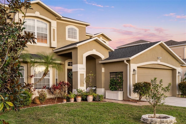 view of front facade with roof with shingles, stucco siding, a lawn, driveway, and an attached garage