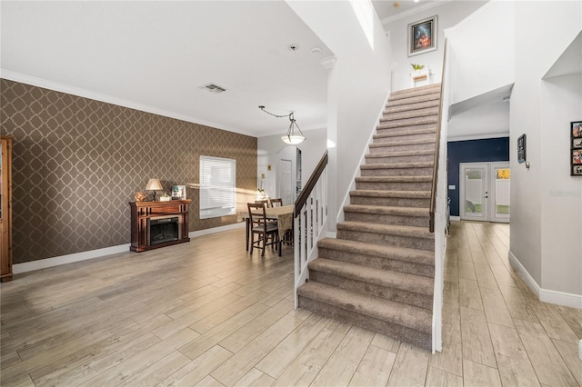 stairs with wallpapered walls, crown molding, baseboards, and wood finished floors