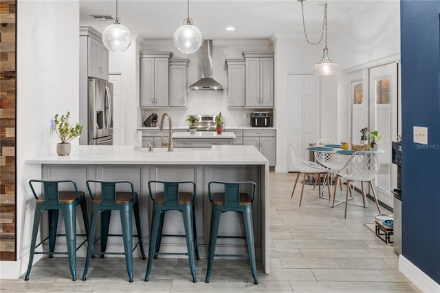 kitchen featuring a kitchen bar, gray cabinets, appliances with stainless steel finishes, and wall chimney exhaust hood