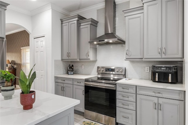 kitchen with arched walkways, gray cabinets, wall chimney exhaust hood, and electric stove