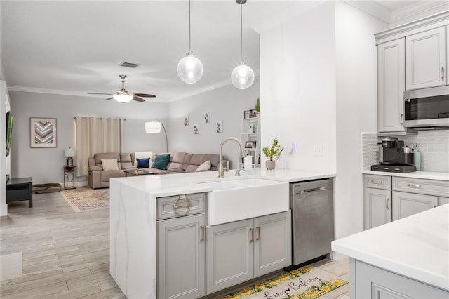 kitchen featuring ornamental molding, gray cabinets, a sink, appliances with stainless steel finishes, and a peninsula