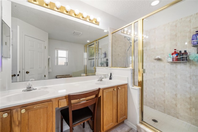 bathroom with visible vents, a shower stall, double vanity, a textured ceiling, and a sink