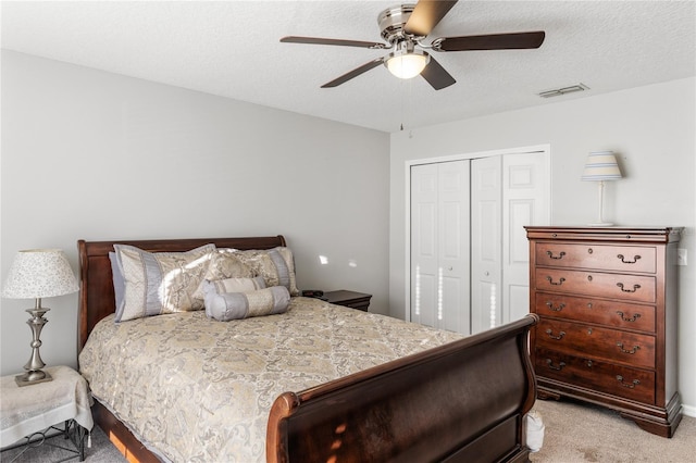 bedroom with visible vents, a textured ceiling, a closet, light colored carpet, and ceiling fan