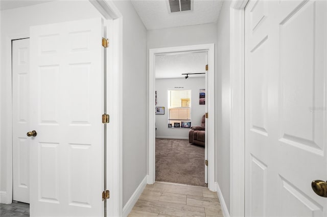 corridor featuring visible vents, baseboards, and a textured ceiling