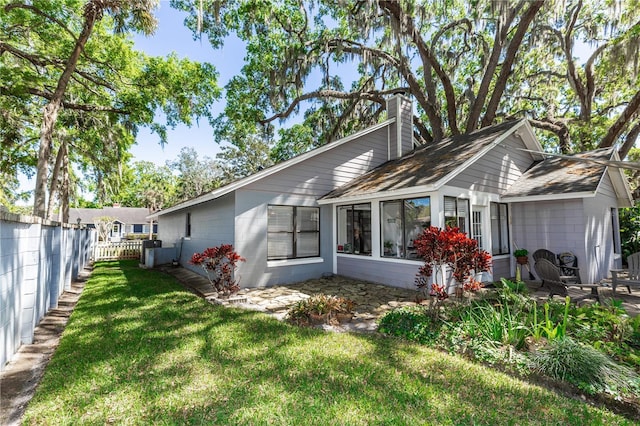 back of property with concrete block siding, a lawn, fence, and a chimney