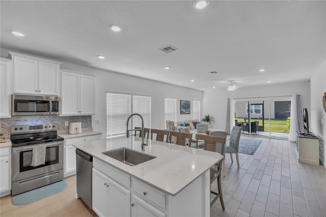 kitchen featuring visible vents, appliances with stainless steel finishes, open floor plan, a sink, and backsplash