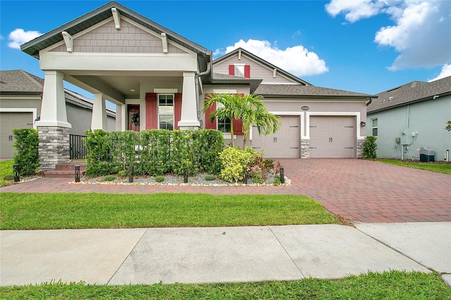 craftsman-style house with decorative driveway, stucco siding, an attached garage, cooling unit, and stone siding