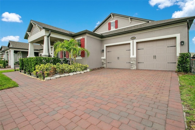 craftsman-style house with an attached garage, stone siding, decorative driveway, and stucco siding