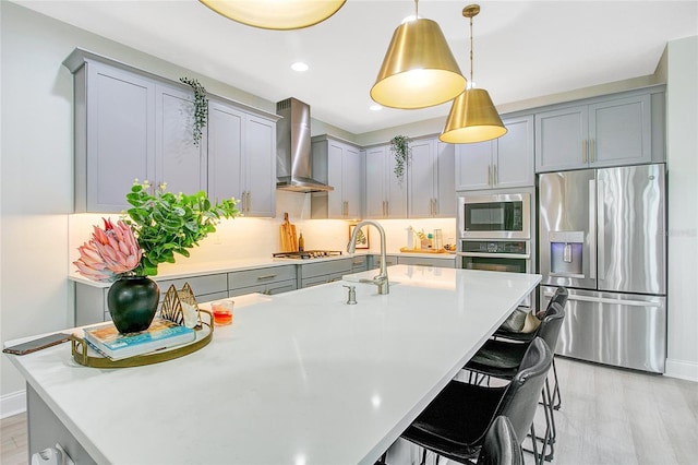 kitchen with a breakfast bar area, stainless steel appliances, light countertops, wall chimney range hood, and gray cabinets