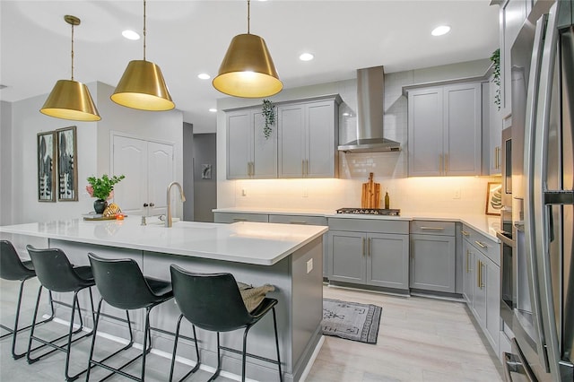 kitchen with decorative backsplash, appliances with stainless steel finishes, gray cabinetry, wall chimney range hood, and a sink