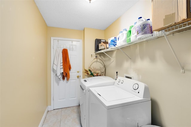 laundry area with light tile patterned floors, washing machine and dryer, a textured ceiling, laundry area, and baseboards