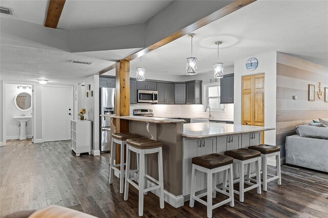 kitchen featuring a kitchen bar, visible vents, backsplash, dark wood finished floors, and stainless steel appliances