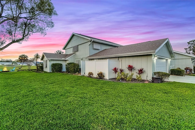 property exterior at dusk featuring a lawn, fence, concrete driveway, an attached garage, and a shingled roof