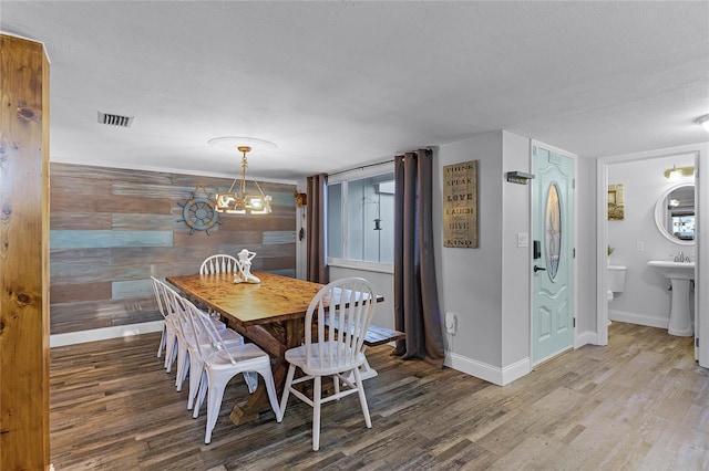 dining area with visible vents, a textured ceiling, wood finished floors, wood walls, and baseboards