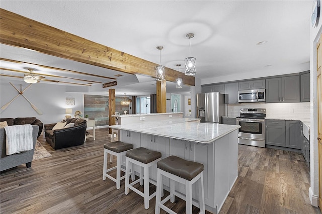 kitchen featuring a breakfast bar area, dark wood finished floors, gray cabinetry, appliances with stainless steel finishes, and backsplash