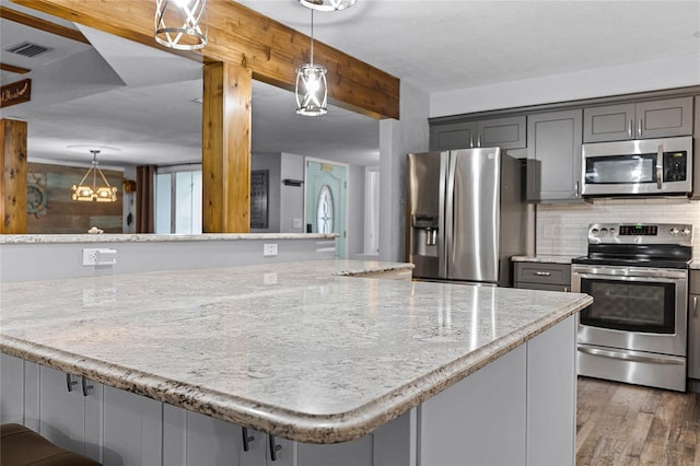 kitchen with gray cabinetry, wood finished floors, stainless steel appliances, decorative backsplash, and light stone countertops