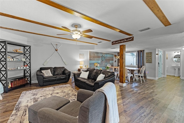 living area with beamed ceiling, visible vents, a ceiling fan, wood finished floors, and baseboards