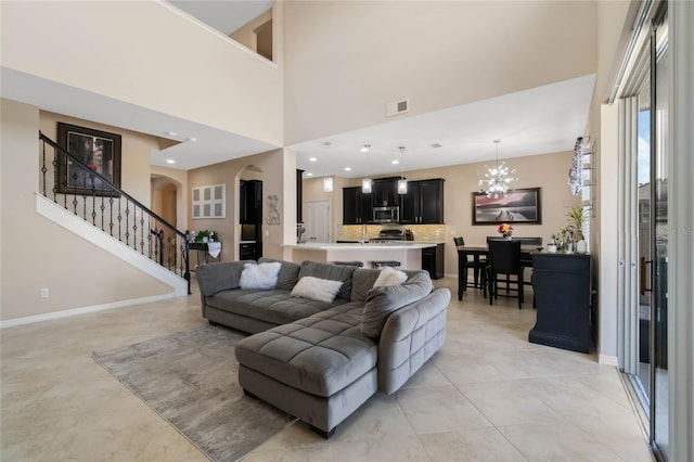 living room with arched walkways, visible vents, baseboards, stairway, and an inviting chandelier