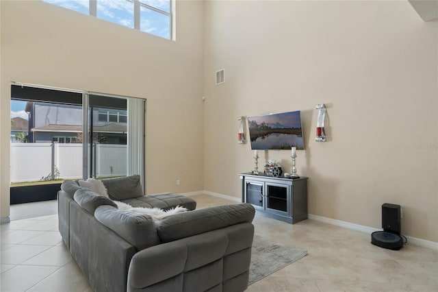 living room featuring a towering ceiling, visible vents, baseboards, and tile patterned floors