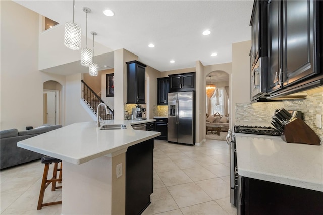 kitchen featuring arched walkways, appliances with stainless steel finishes, a breakfast bar area, a peninsula, and a sink