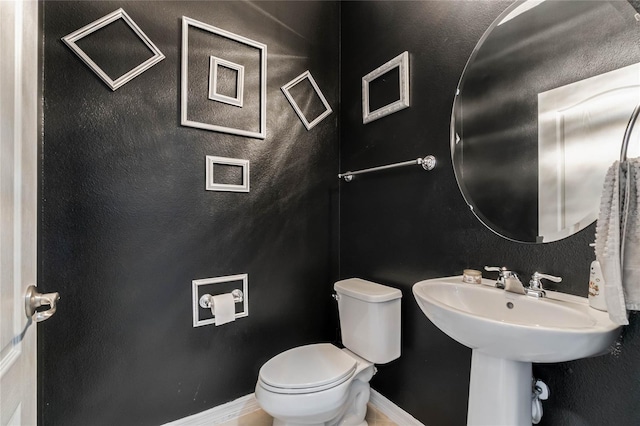 half bath featuring baseboards, a textured wall, and toilet