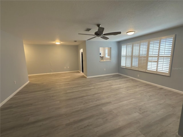 unfurnished room with a ceiling fan, wood finished floors, visible vents, and baseboards