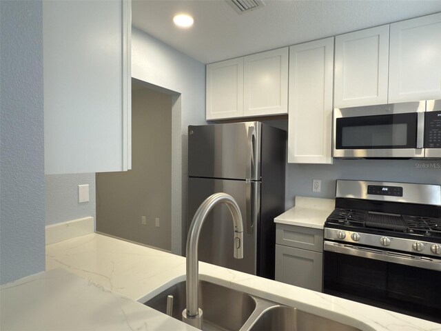 kitchen featuring light stone counters, visible vents, a sink, stainless steel appliances, and white cabinetry