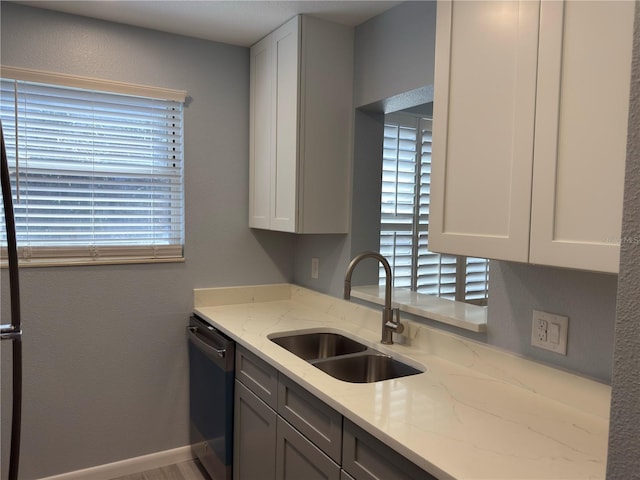 kitchen featuring a sink, white cabinetry, baseboards, dishwashing machine, and light stone countertops